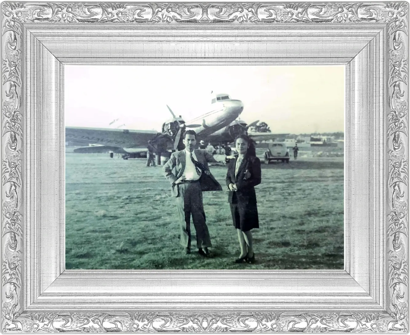 Lidia y Luis, de traje, posando sobre el pasto de una pista frente a un avión de hélice