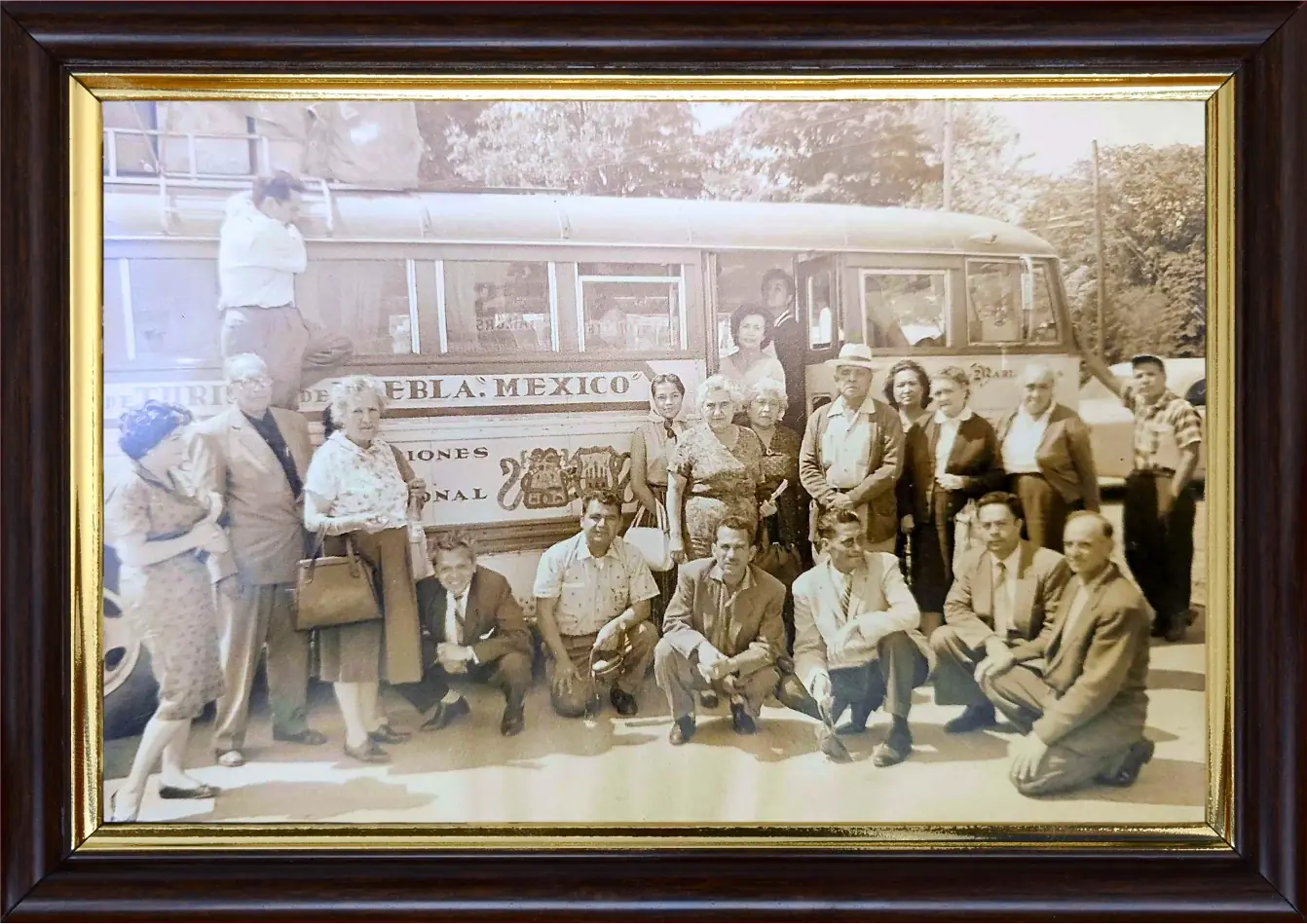 Grupo de una quincena de viajeros posando frente a un autobús rotulado «Puebla, México», con un hombre de pie sobre la parrilla del techo
